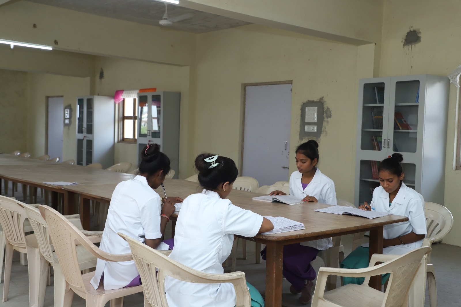 person writing in a notebook beside by an iPad, laptop, printed photos, spectacles, and a cup of coffee on a saucer