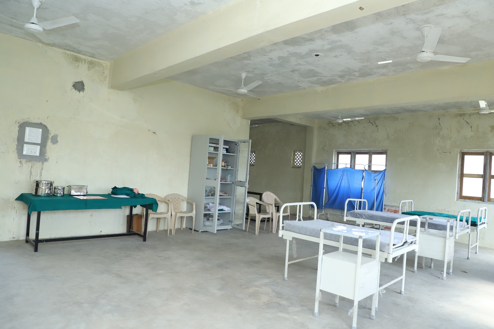 person writing in a notebook beside by an iPad, laptop, printed photos, spectacles, and a cup of coffee on a saucer