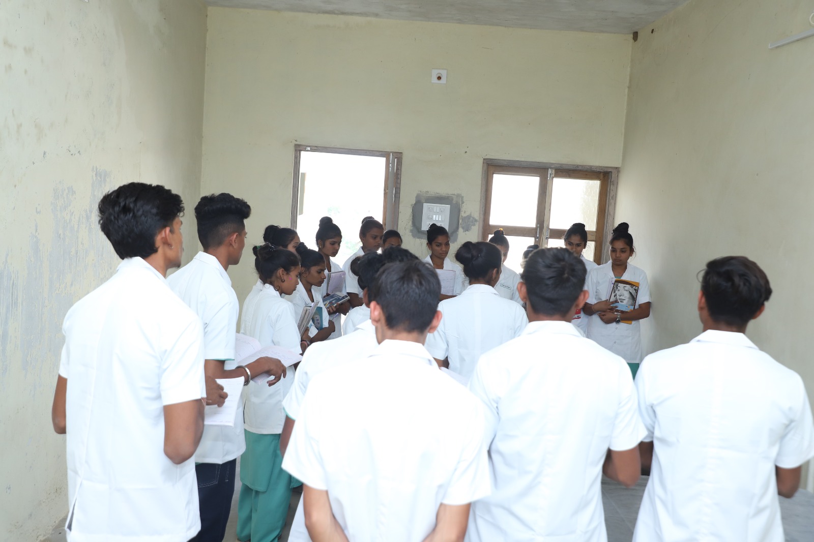 person writing in a notebook beside by an iPad, laptop, printed photos, spectacles, and a cup of coffee on a saucer