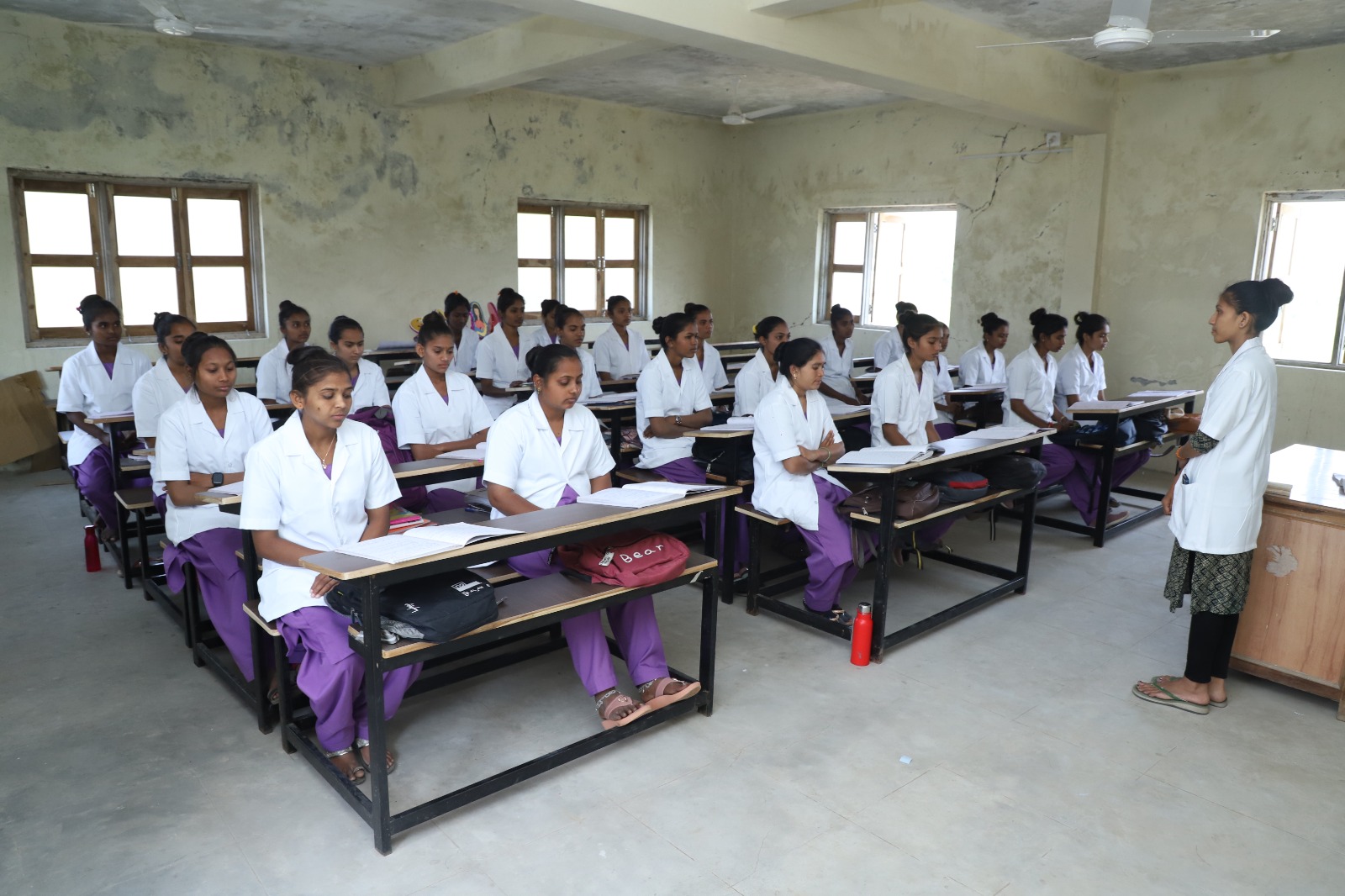 person writing in a notebook beside by an iPad, laptop, printed photos, spectacles, and a cup of coffee on a saucer
